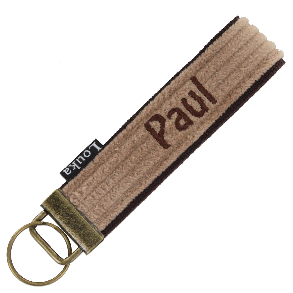 Handgemaakte Louka pols sleutelhanger van brede rib in camel, personaliseerbaar met naam en verkrijgbaar met zilver of brons hardware, formaat 13×3 cm.